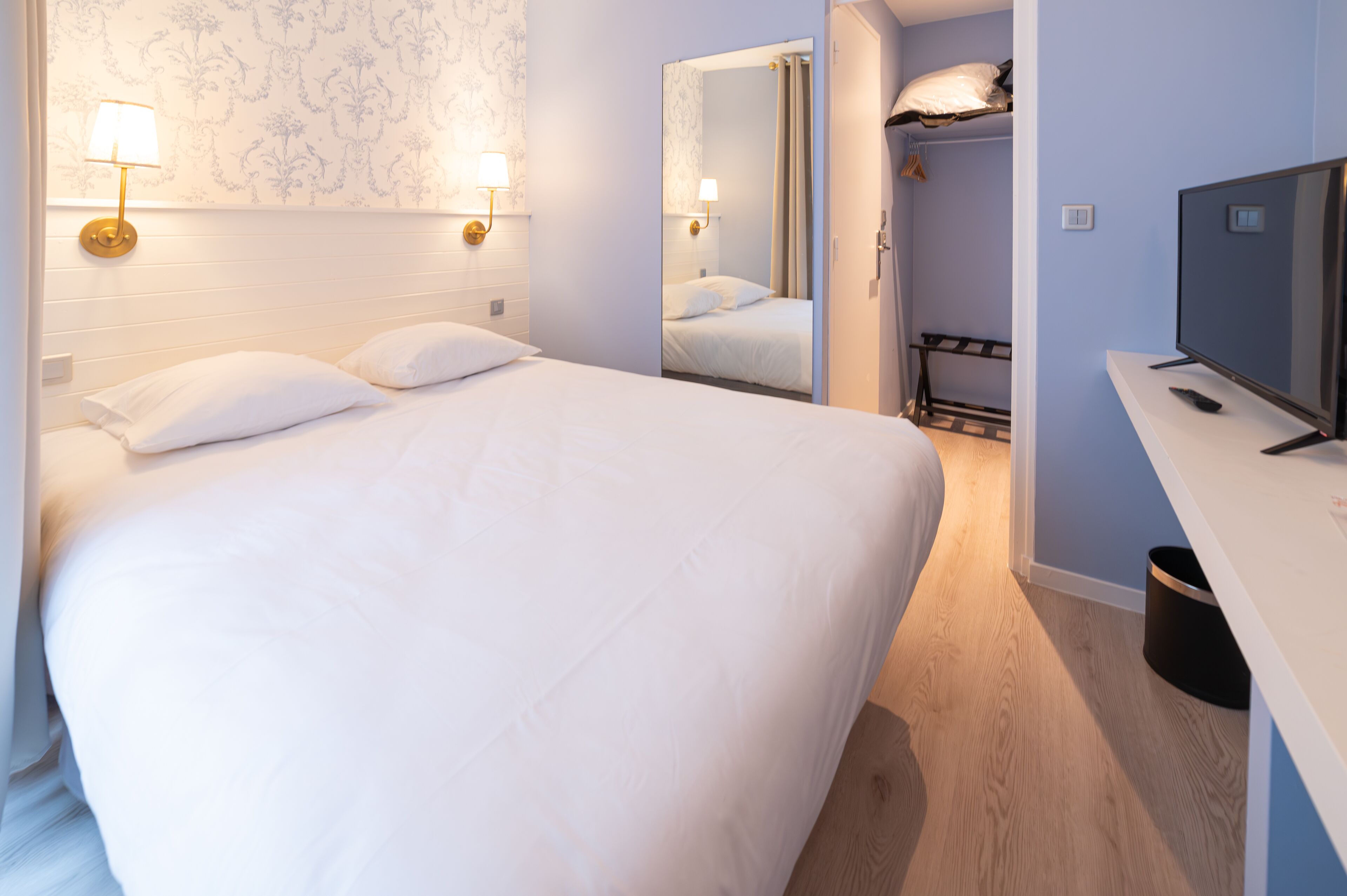 A hotel room with a large bed, bedside lamps, a TV, and a mirror.