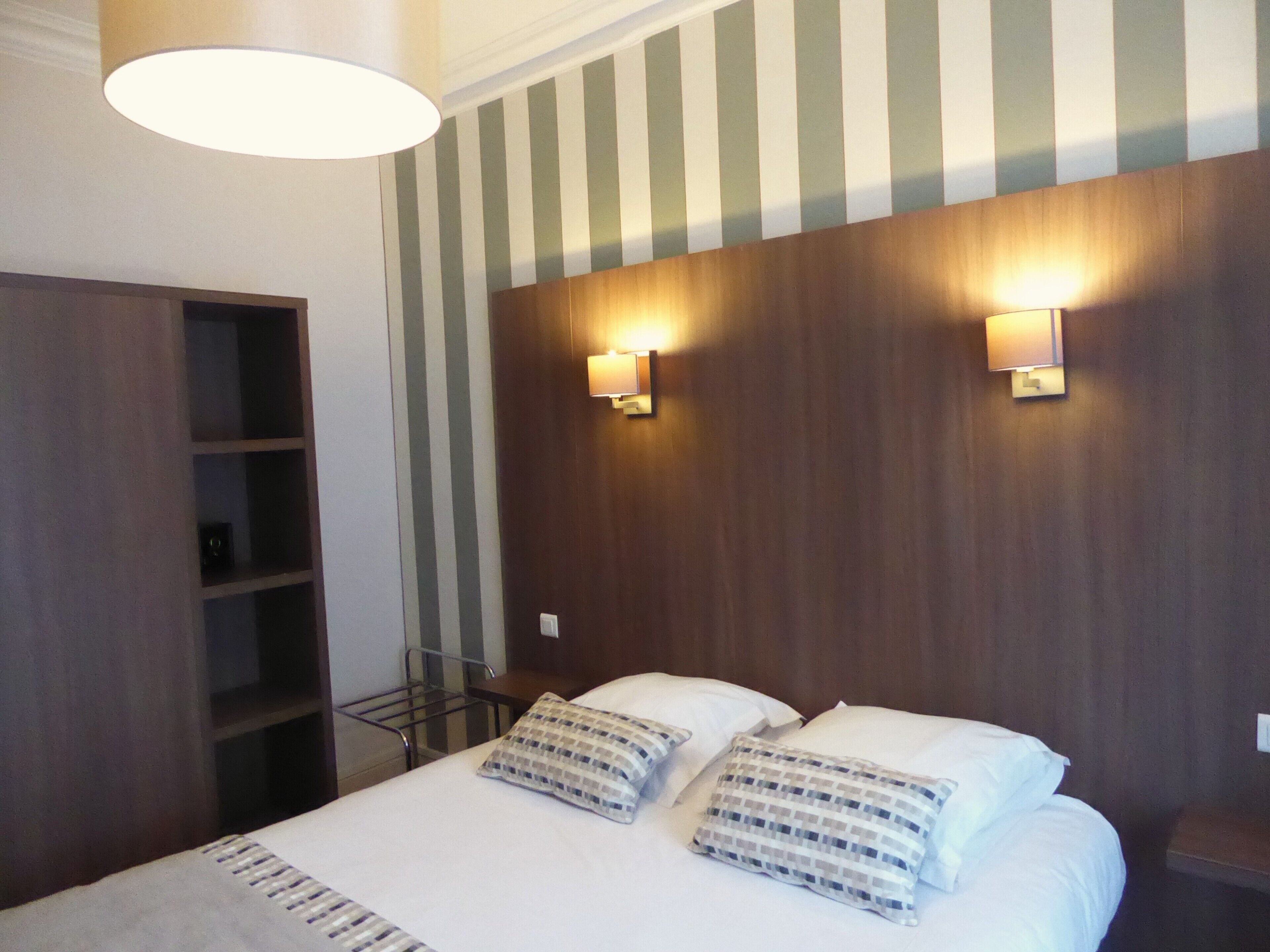 A hotel room with a bed, two bedside lamps, a wooden headboard, and a striped wall.