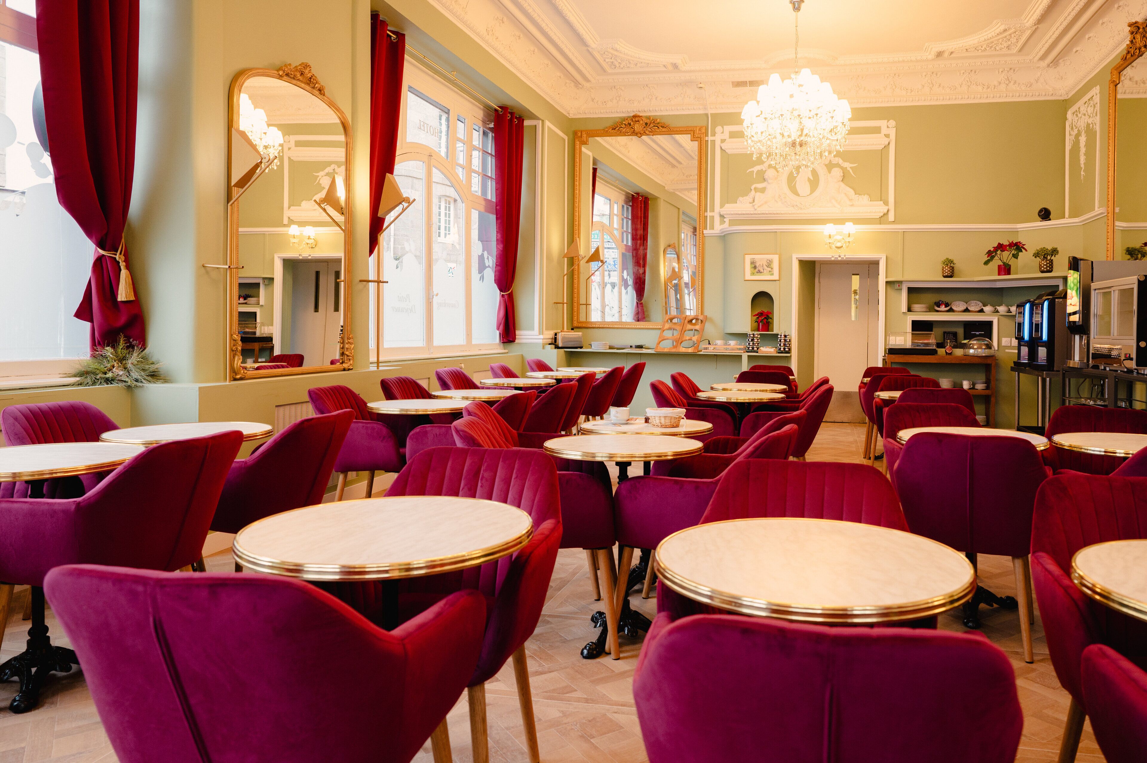 A dining area with round tables and red upholstered chairs, large mirrors, and a chandelier.