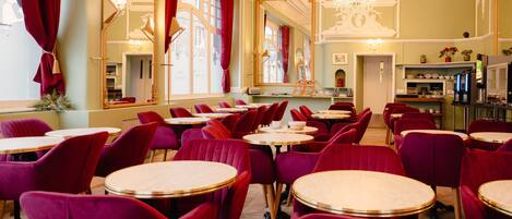 A dining area with round tables and red upholstered chairs, large mirrors, and a chandelier.