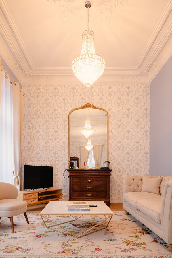Un salón con candelabro, un espejo grande, televisor, mesa de centro y sofá.