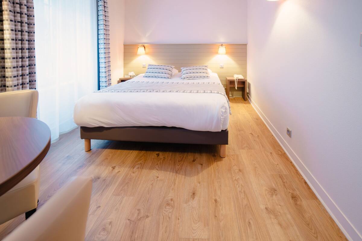 Une chambre bien rangée, avec un grand lit, des lampes de chevet, une petite table et une chaise.