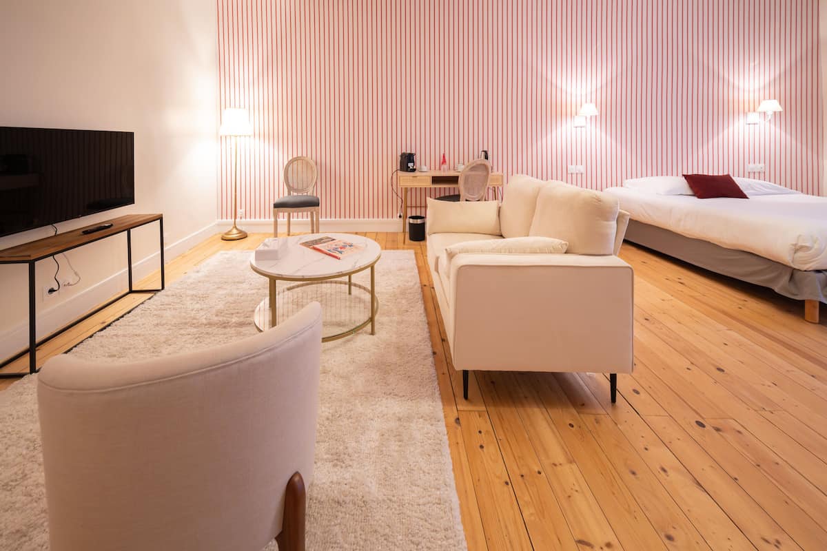 Une chambre d’hôtel moderne équipée d’un téléviseur à écran plat, d’un canapé, d’une table basse, d’un bureau et d’un lit avec un oreiller rouge.