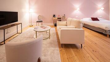 A modern hotel room with a flat-screen TV, a sofa, a coffee table, a desk, and a bed with a red pillow.