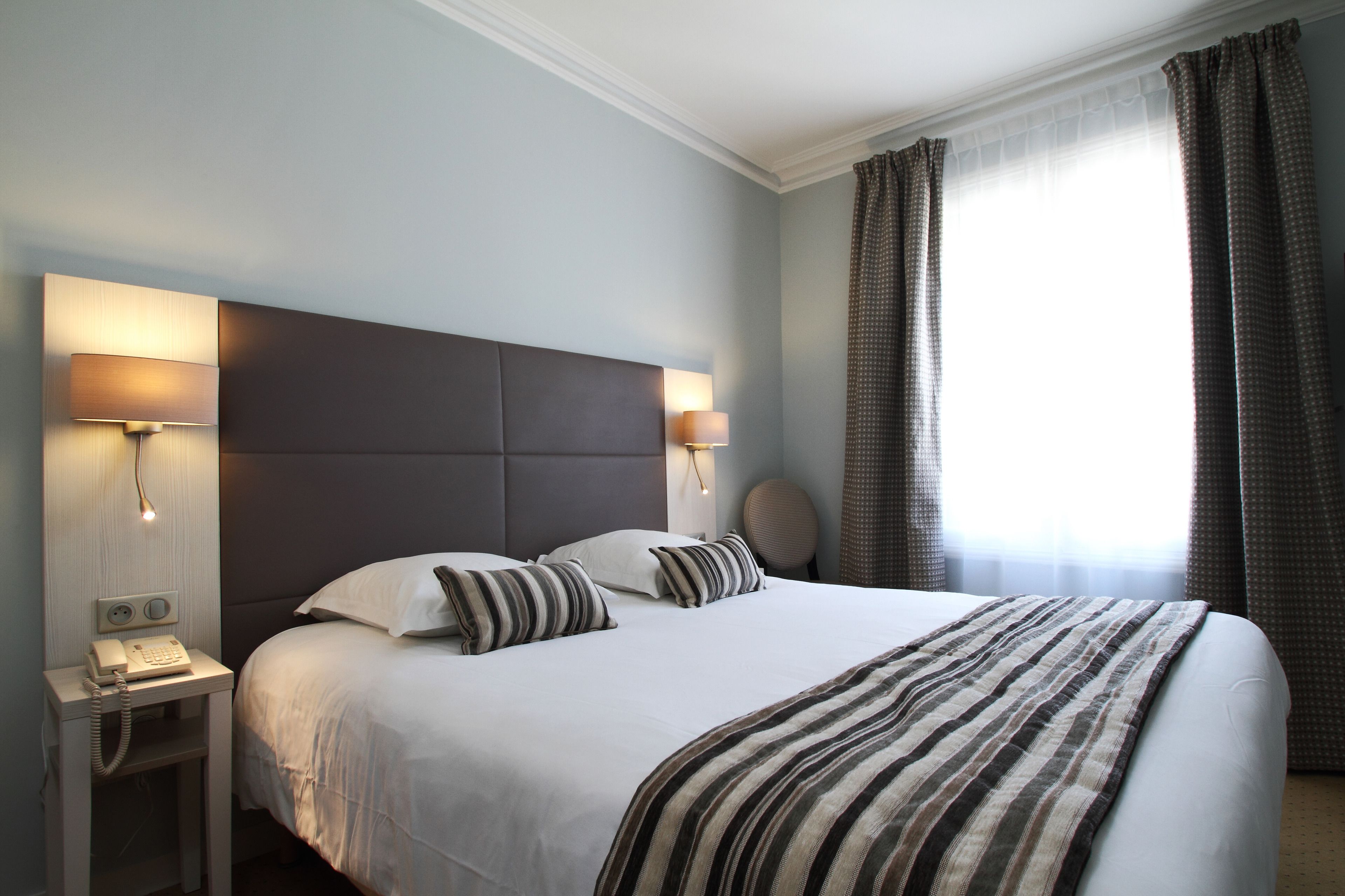 A hotel room with a large bed, two bedside lamps, a telephone, and a round wall clock.