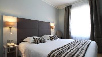 A hotel room with a large bed, two bedside lamps, a telephone, and a round wall clock.