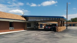 A motel with a brick facade, a covered parking area, and a car parked in front.