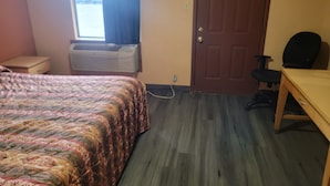 A bedroom with a bed, a desk, a chair, an air conditioning unit, a door, and a window.