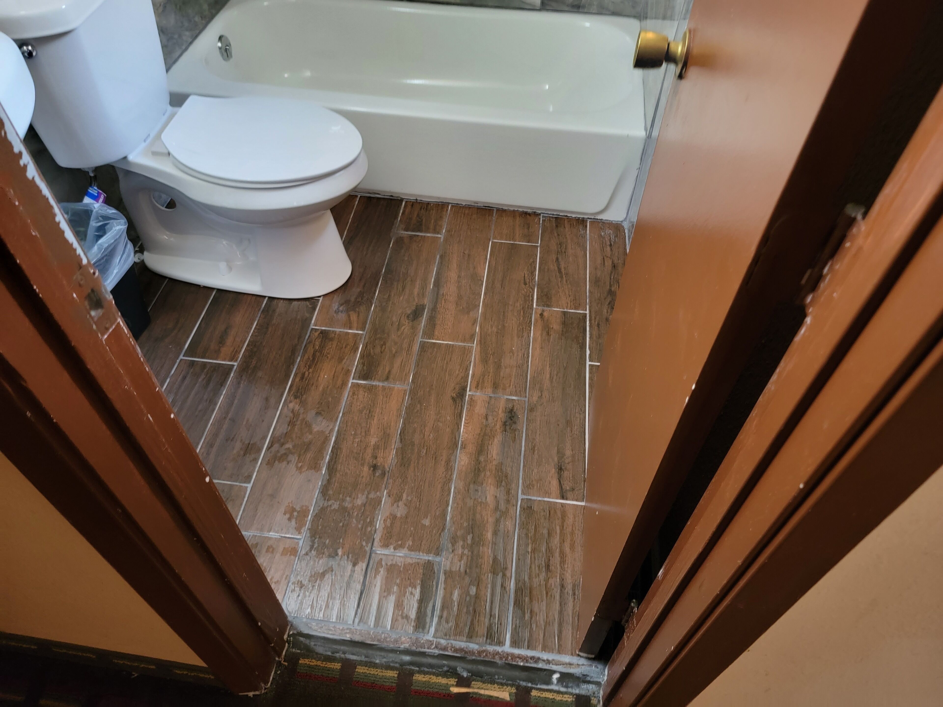 A bathroom with a toilet, bathtub, and wooden floor.