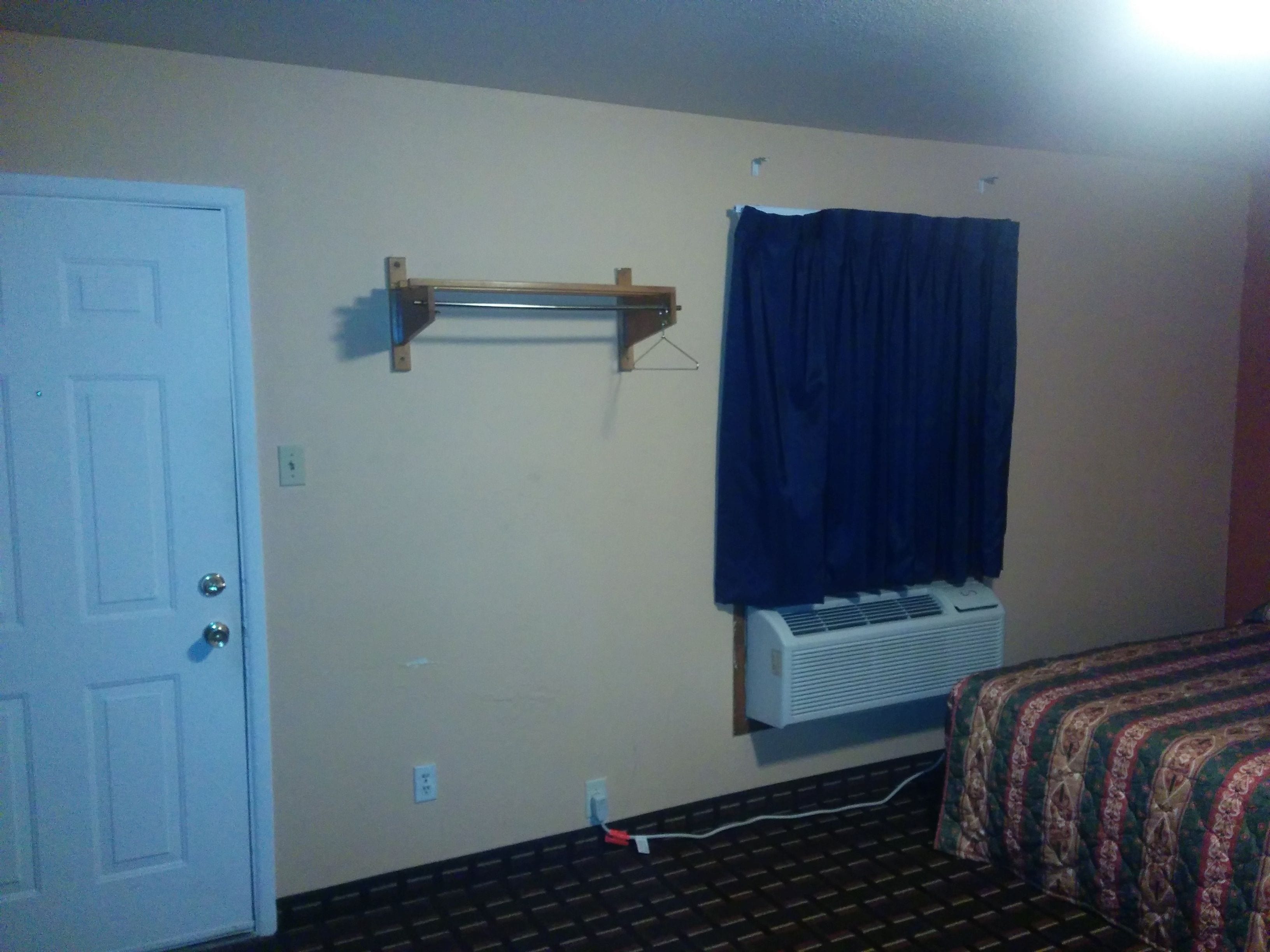 A room with a bed, a wall-mounted air conditioner, a door, and a curtain.