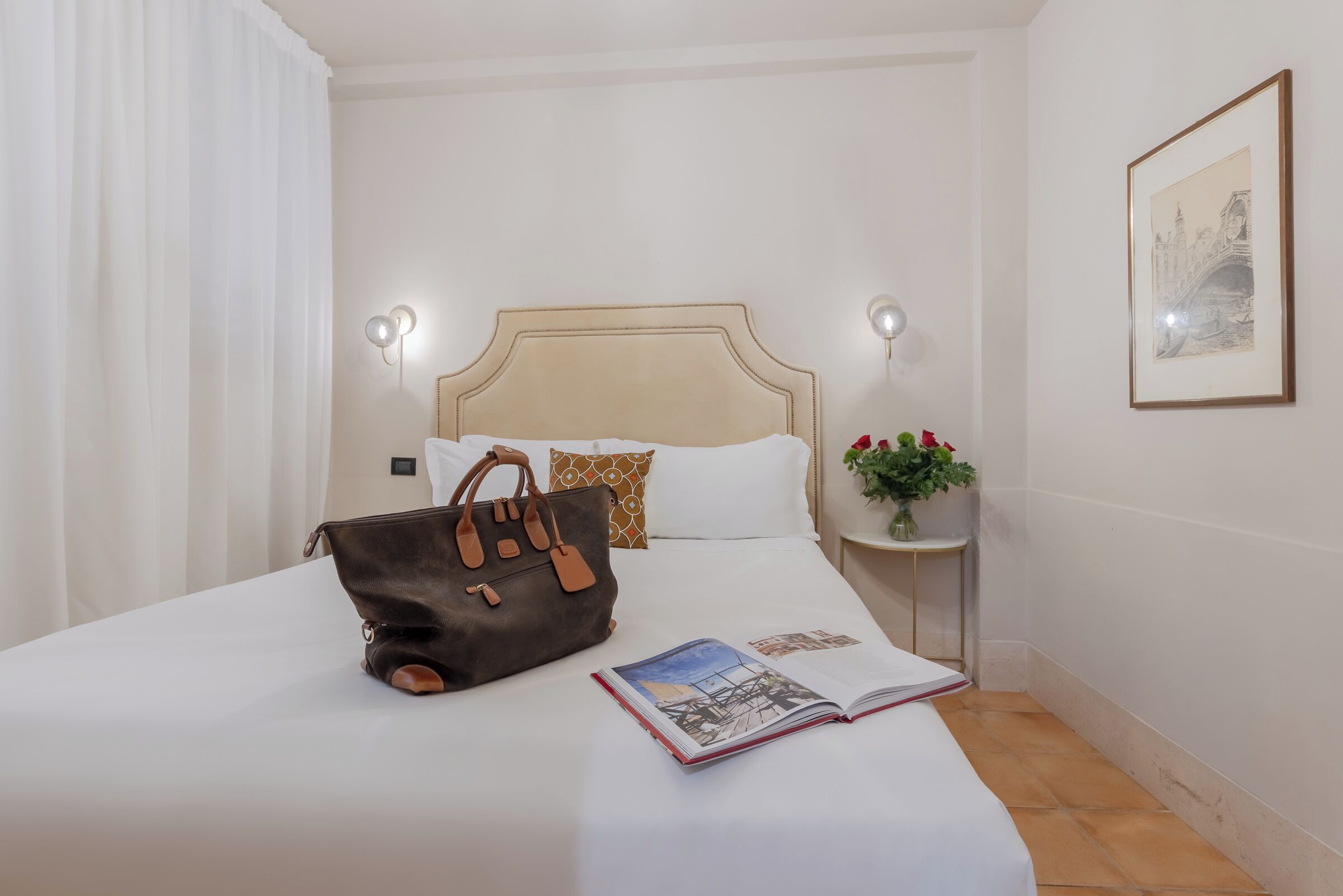 Een opgemaakt bed met een bruine leren tas en een open tijdschrift erop.