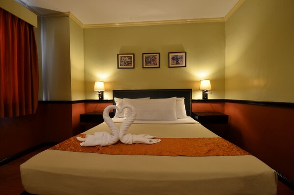 A hotel room with a large bed, two bedside lamps, and a heart-shaped towel arrangement. - Fernandina 88 Suites Hotel (QUEZON CITY)