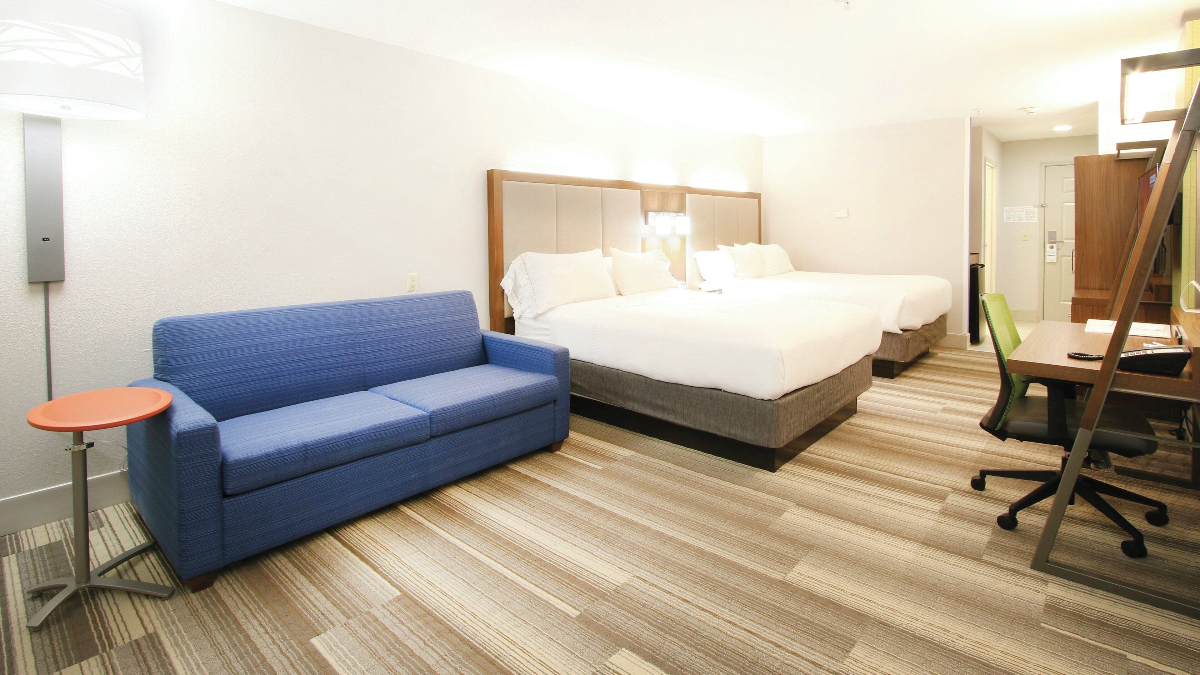 A hotel room with a blue sofa, a bed with white linens, a small table, and a desk with a chair.