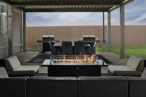 Un patio al aire libre con una chimenea, dos parrillas de barbacoa, mobiliario de mimbre y una valla de madera al fondo.