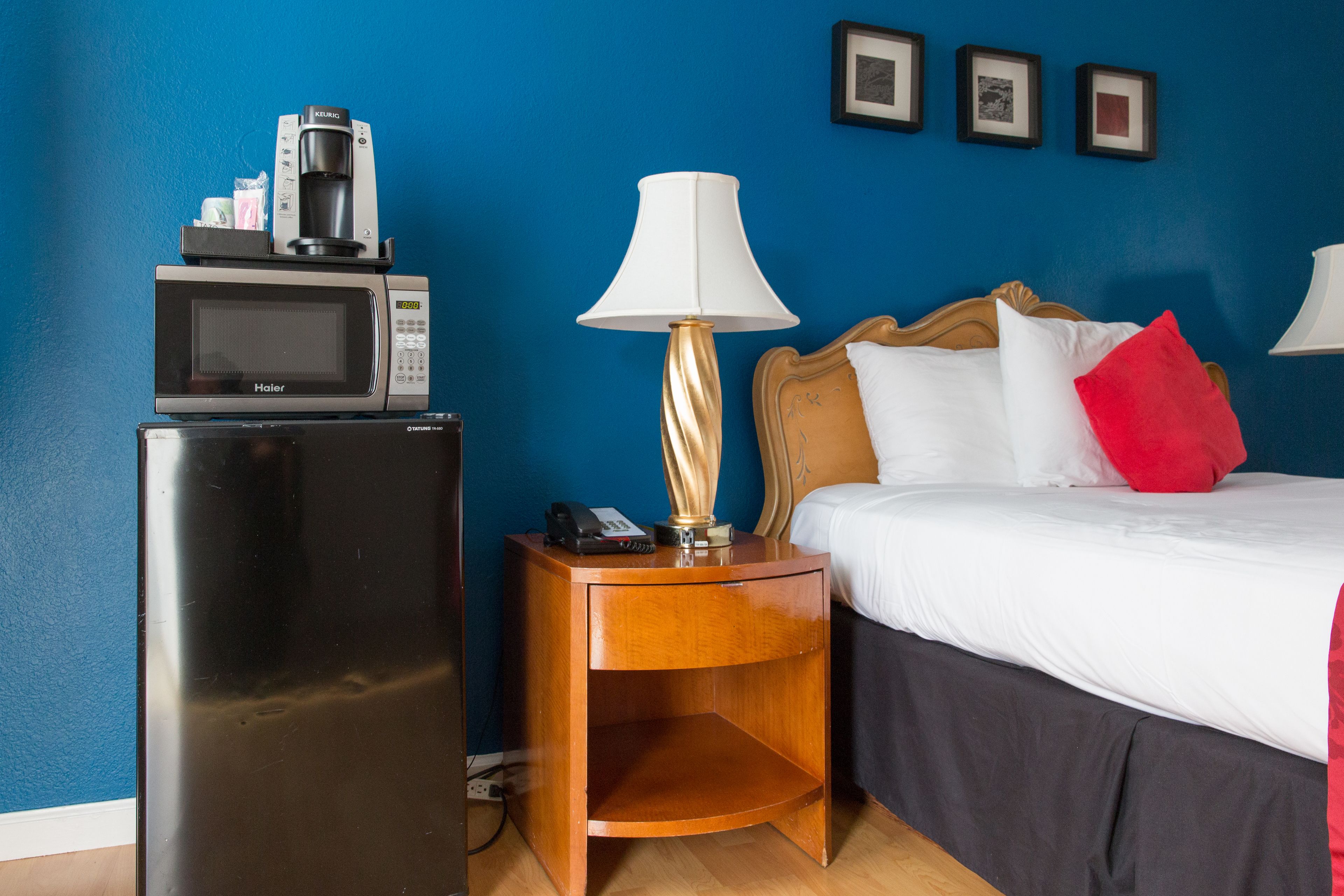 Una habitación de hotel con una cama, una mesita de noche con lámpara, un microondas y una cafetera.