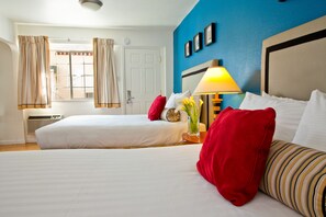 A hotel room with two beds, a nightstand with a lamp, and a window with curtains.