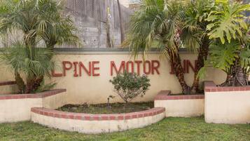 Placa do 'Pine Motor Inn' com um jardim ajardinado, apresentando palmeiras e um pequeno arbusto.