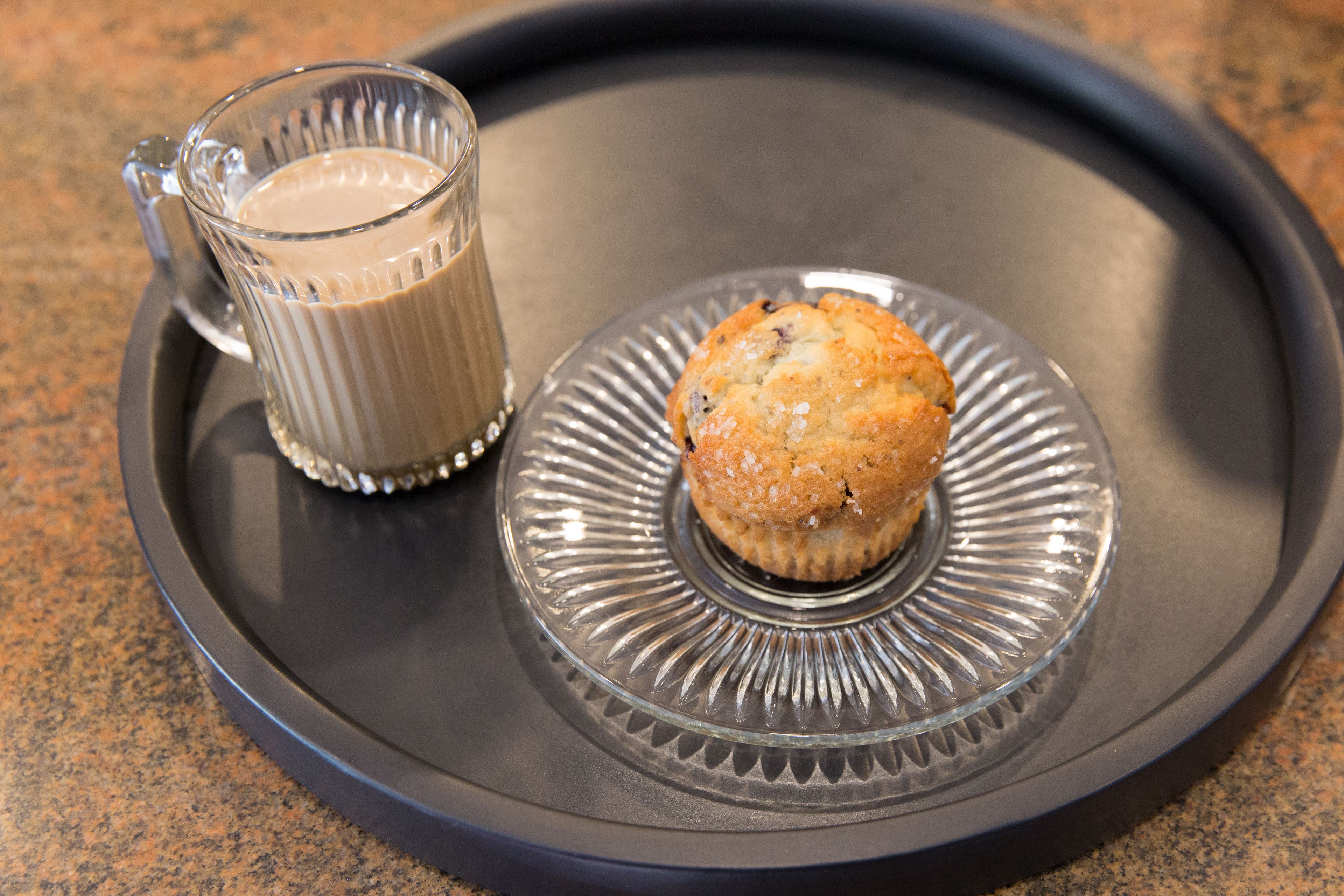 A clear glass mug with a handle and a muffin on a plate with a decorative rim.
