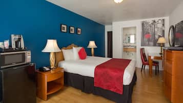 A hotel room with a bed, a desk, a chair, a microwave, a refrigerator, and a lamp.