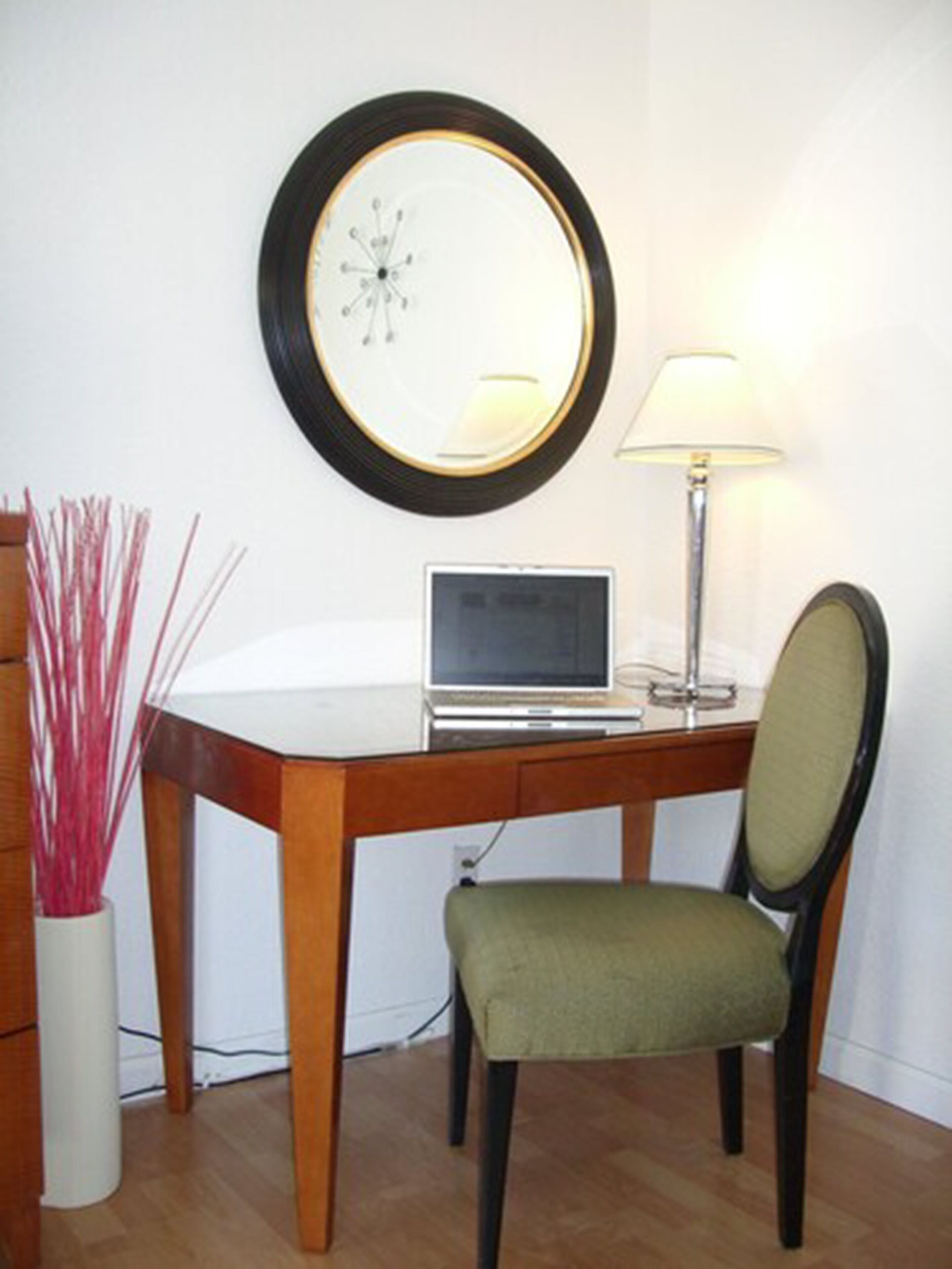 Un petit bureau comprenant un bureau, une chaise, une lampe et une horloge fixée au mur.
