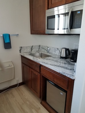 A compact kitchen with a stainless steel microwave, a built-in sink, and a coffee maker.