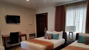 A hotel room with two beds, a desk, a chair, a TV, and a window with curtains.