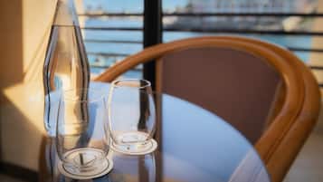 Una mesa con una botella y dos vasos, una silla de madera, y una vista de un puente y edificios a través de una ventana.