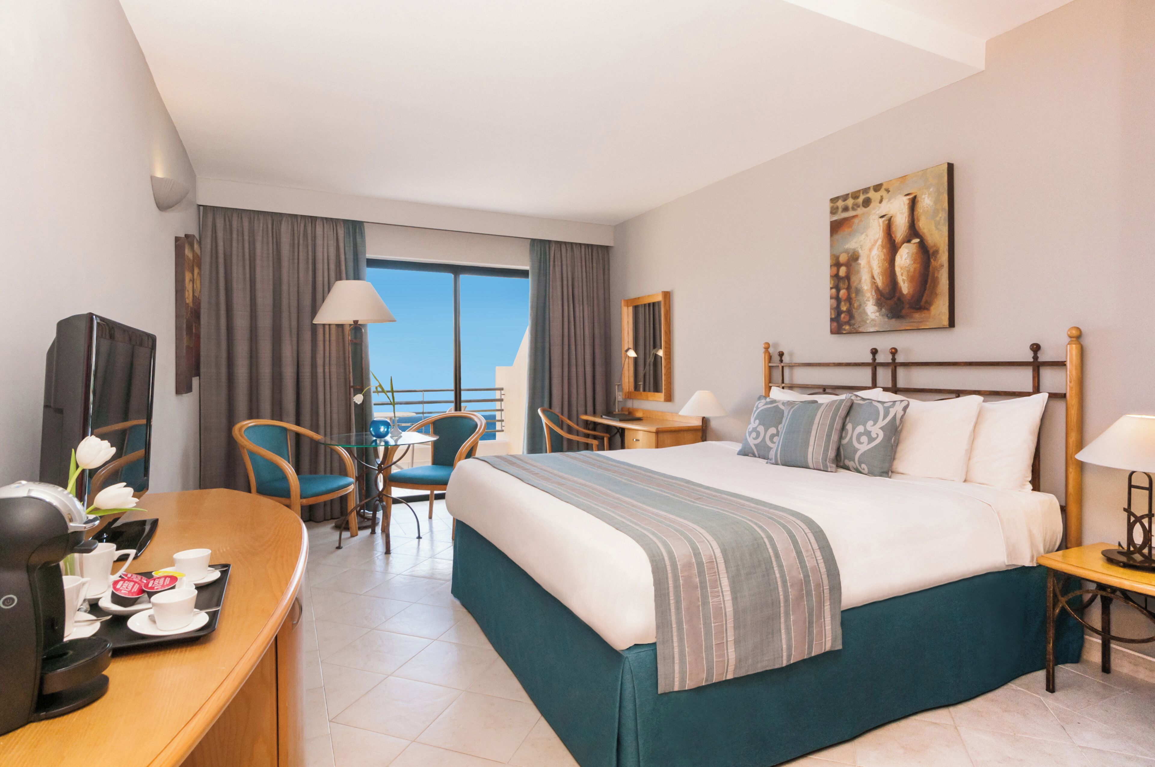 A hotel room with a bed, a desk with a coffee maker, a chair, a table, and a view of the outside.