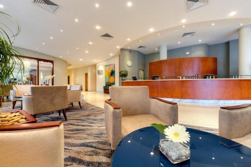 A hotel lobby with a reception desk, seating area, and a large plant.
