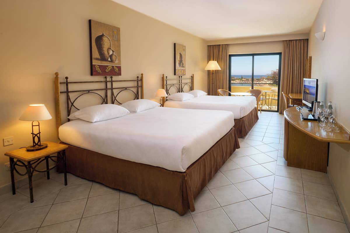 A hotel room with two beds, a desk with a computer, a chair, and a view of the city through the window.