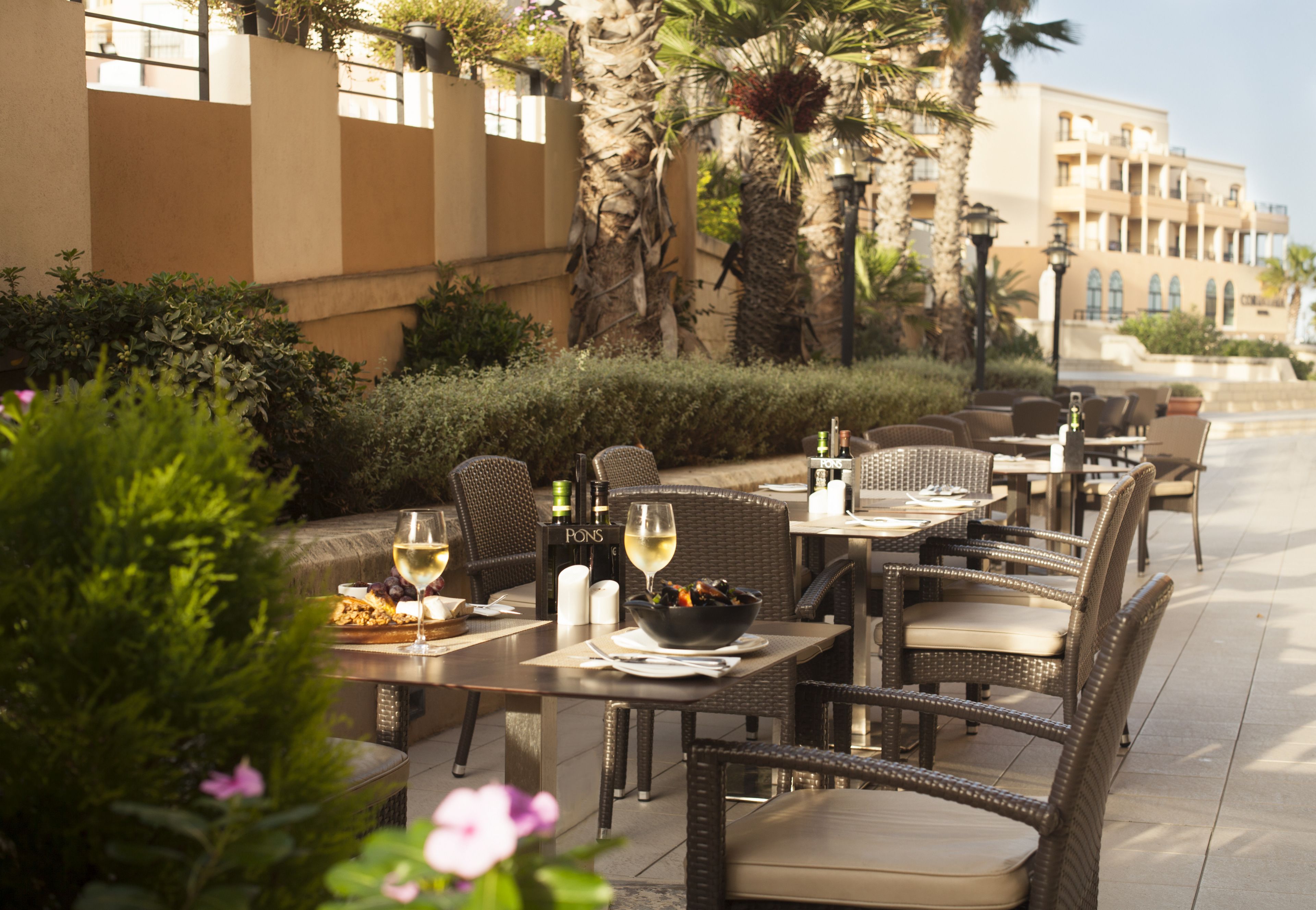 An outdoor dining area with wicker furniture, a bowl of food, and a bottle of wine on a table.