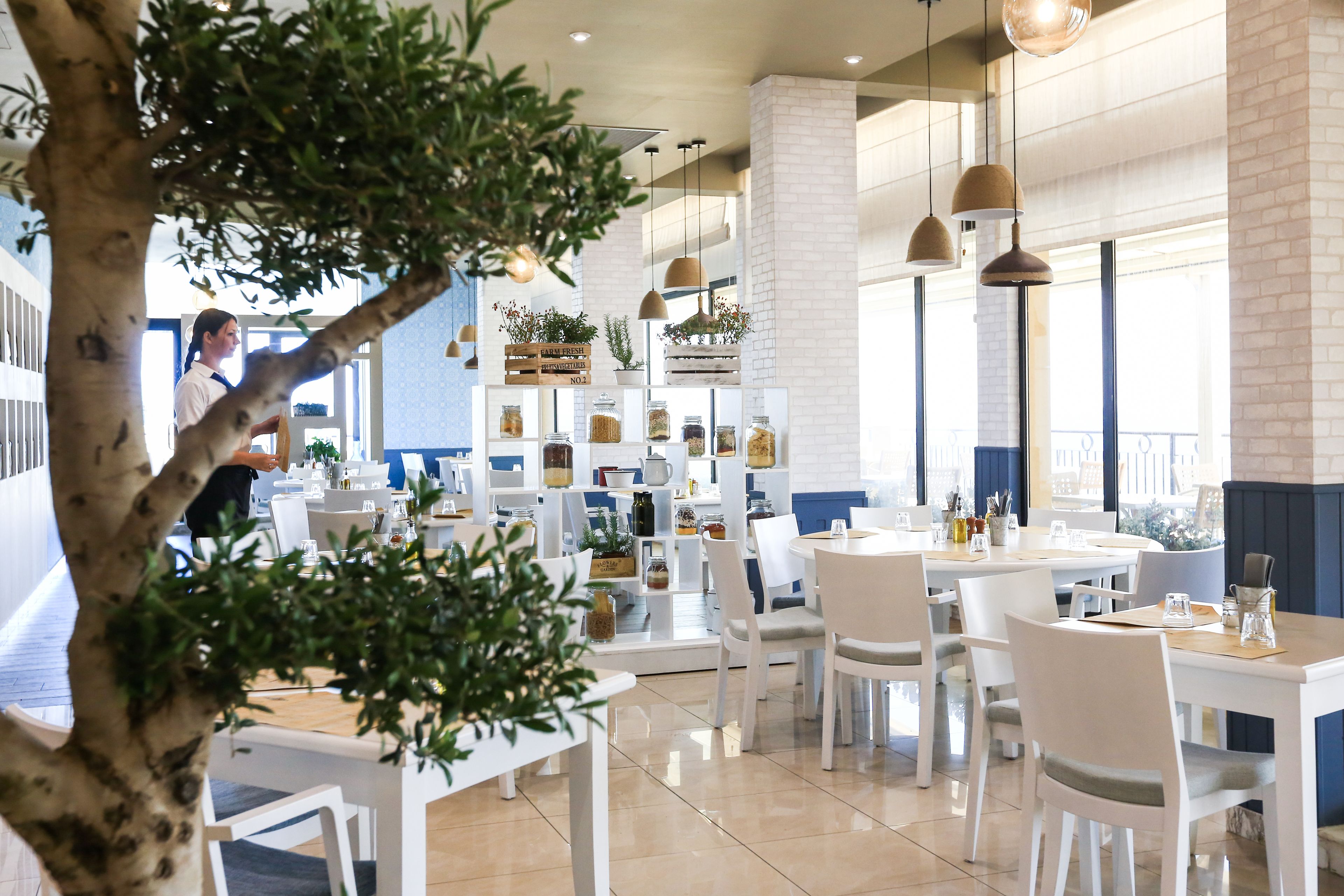 A restaurant with white tables and chairs, hanging pendant lights, and a brick wall.