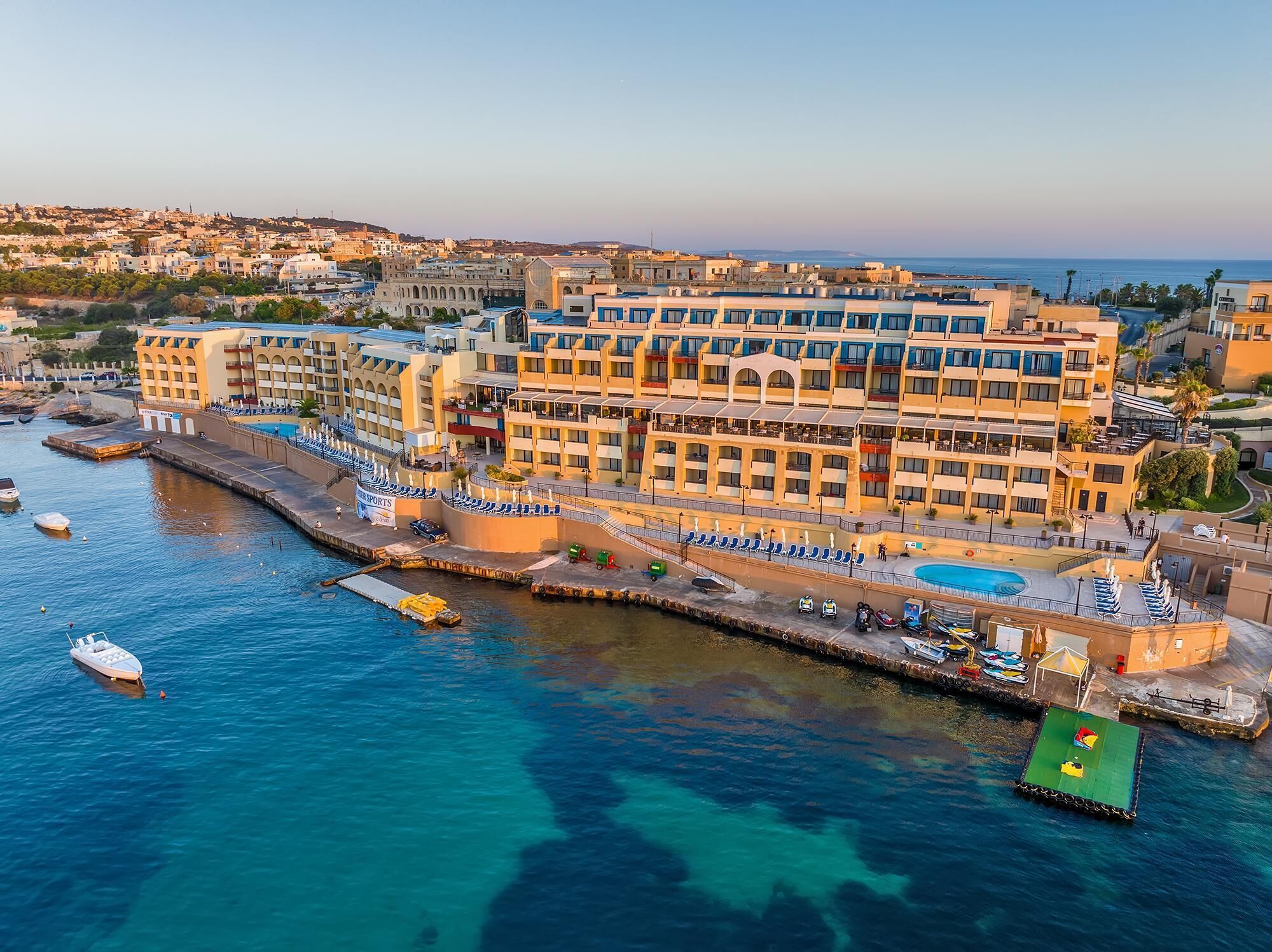 Un hotel frente al mar con un puerto deportivo, varios balcones y una piscina.