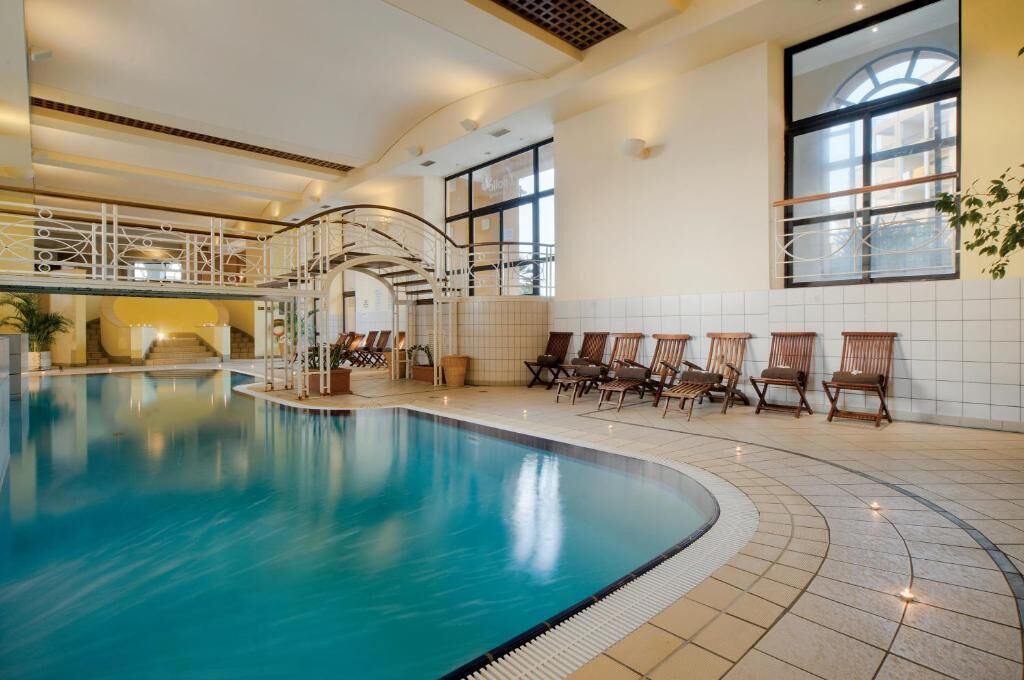 An indoor swimming pool with a curved edge, a staircase, and lounge chairs along the wall.