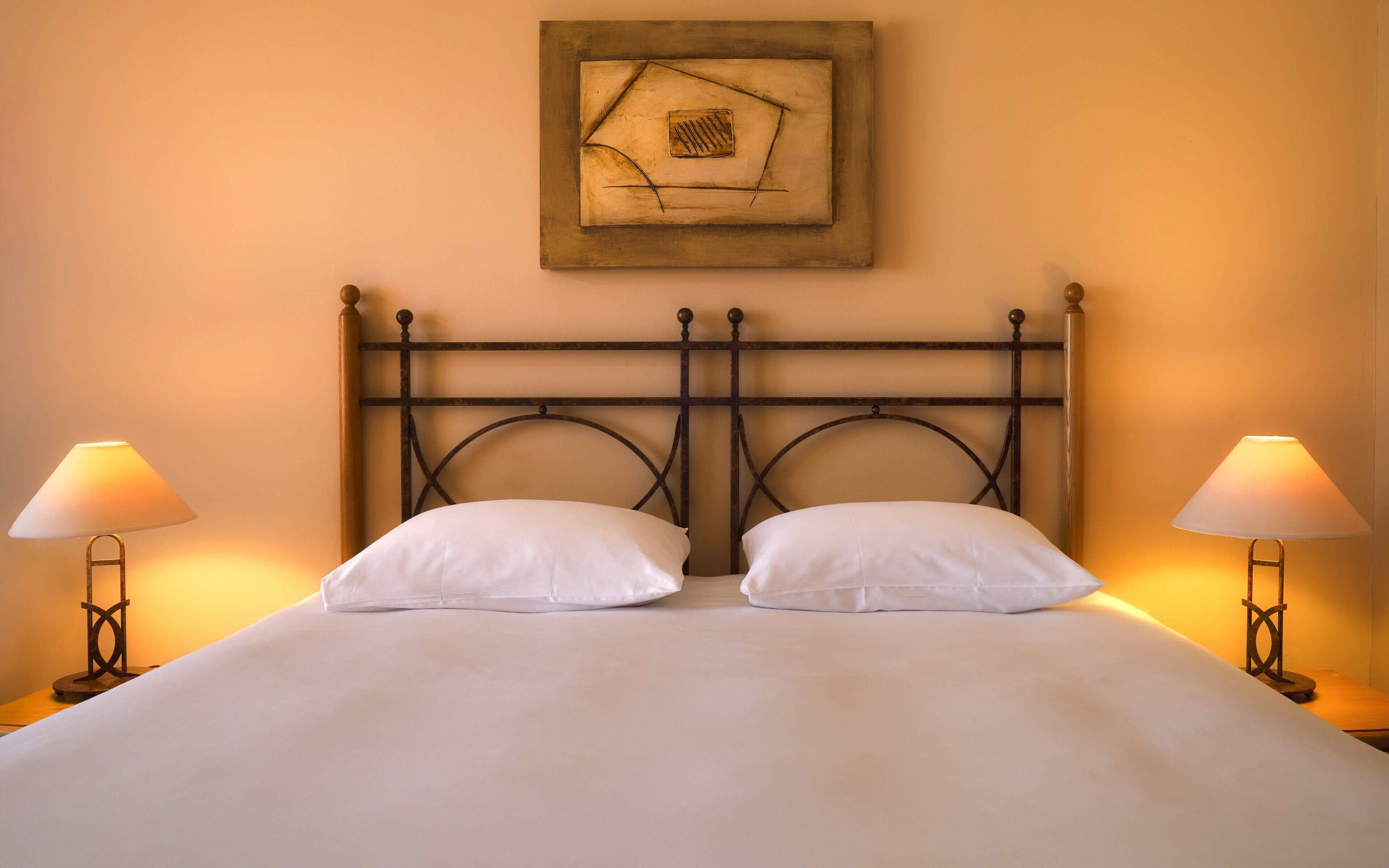 A bed with a metal headboard, two bedside lamps, and a framed artwork above the bed.