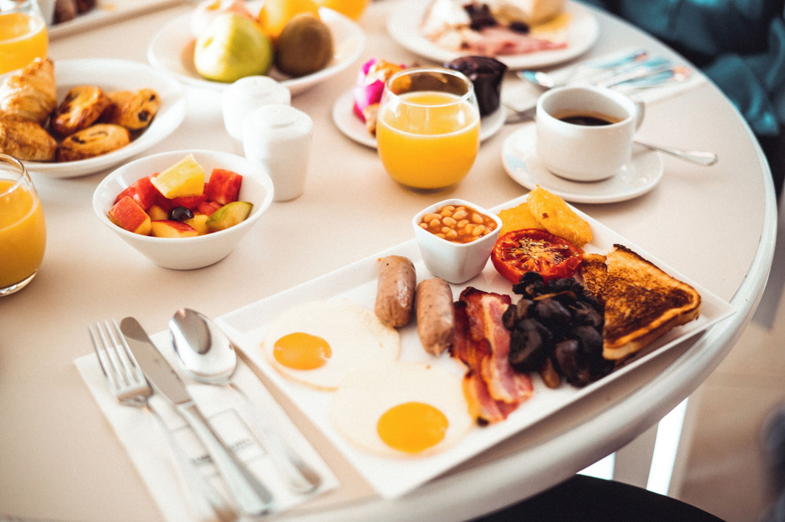 A breakfast table with plates of eggs, sausages, toast, and various fruits and beverages.