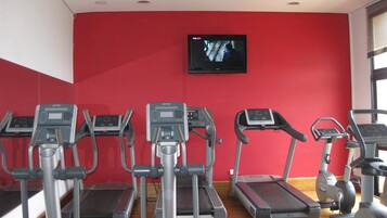 Ein Fitnessstudio mit Laufbändern, Crosstrainern und einem Fernseher an der Wand.