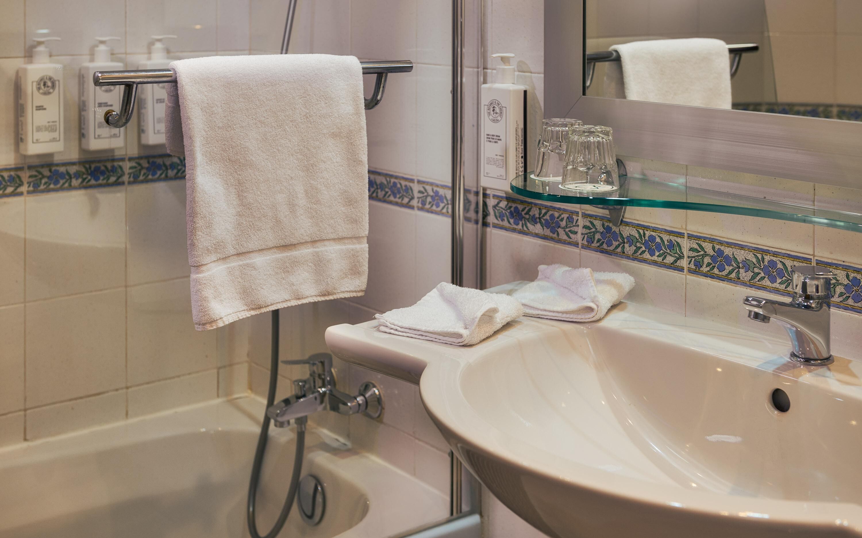 A bathroom with a bathtub, a sink, a glass shower enclosure, and a mirror.