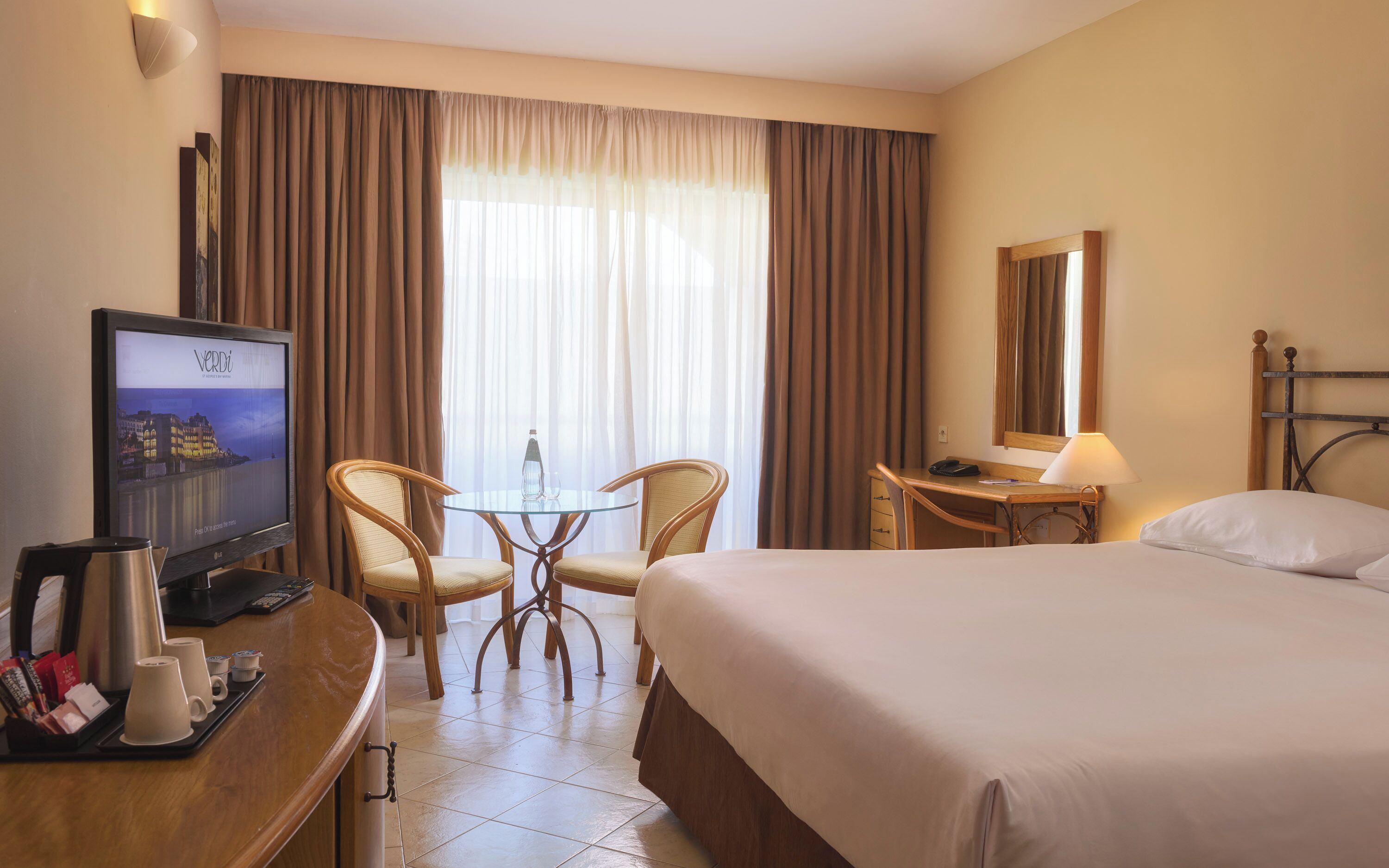 Ein Hotelzimmer mit einem Bett, einem Schreibtisch mit Stuhl, einem Fernseher und einem Fenster mit Vorhängen.
