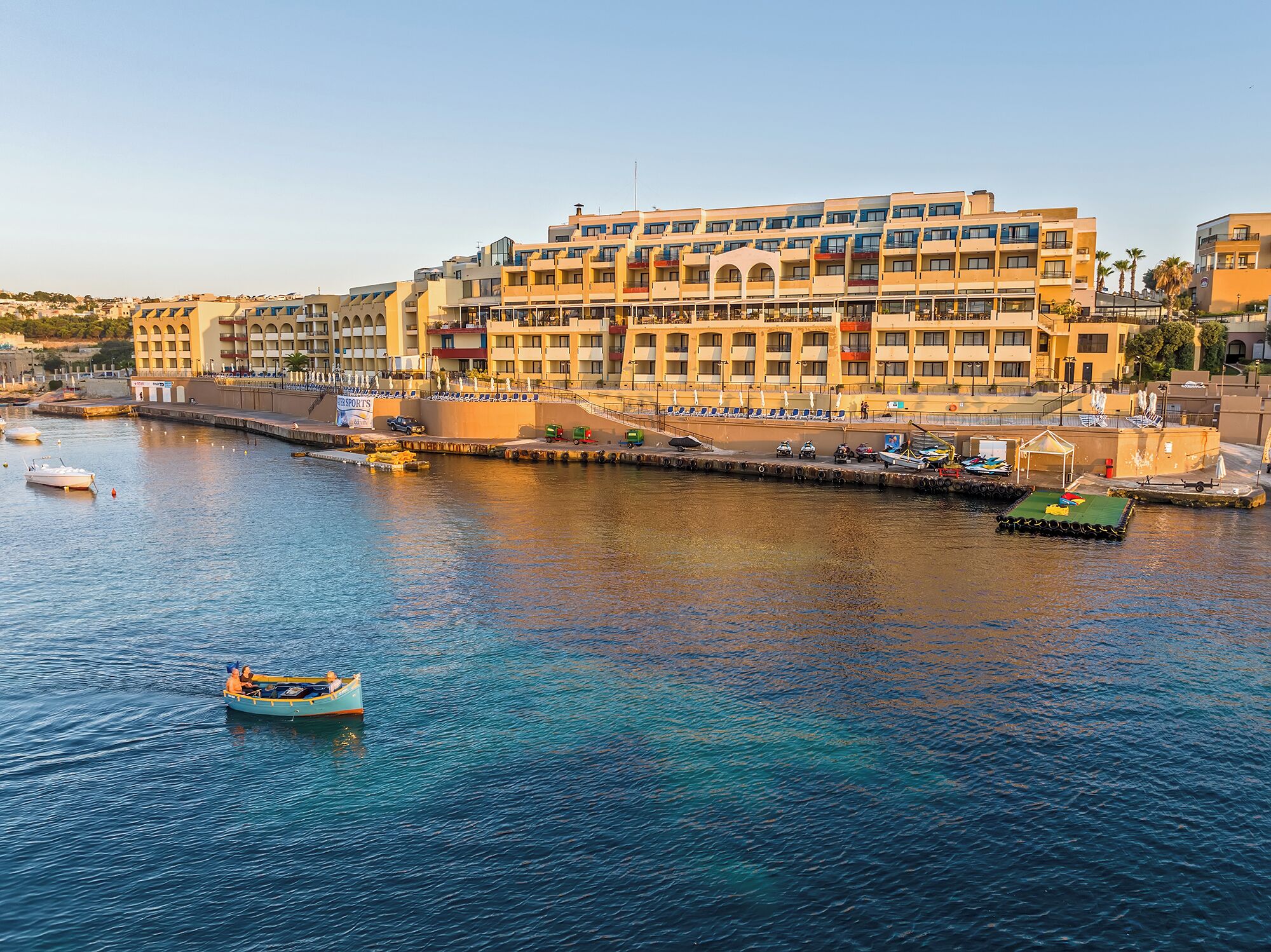 Un hôtel situé au bord de l’eau, doté de nombreux balcons, d’un port de plaisance avec des bateaux et offrant une vue dégagée sur la mer.