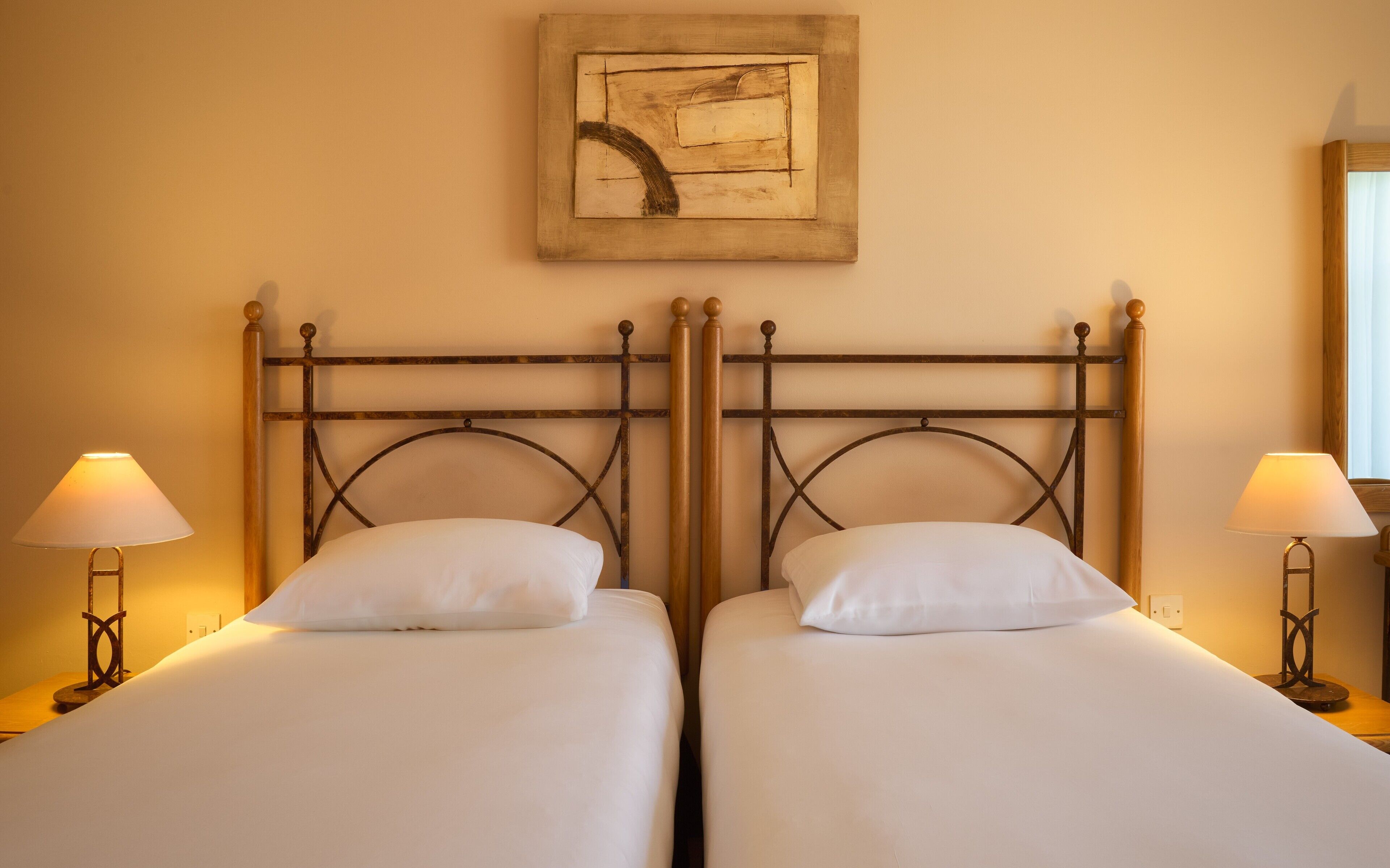 Une chambre d’hôtel avec deux lits simples, chacun doté d’une tête de lit en bois et d’une table de chevet avec une lampe.