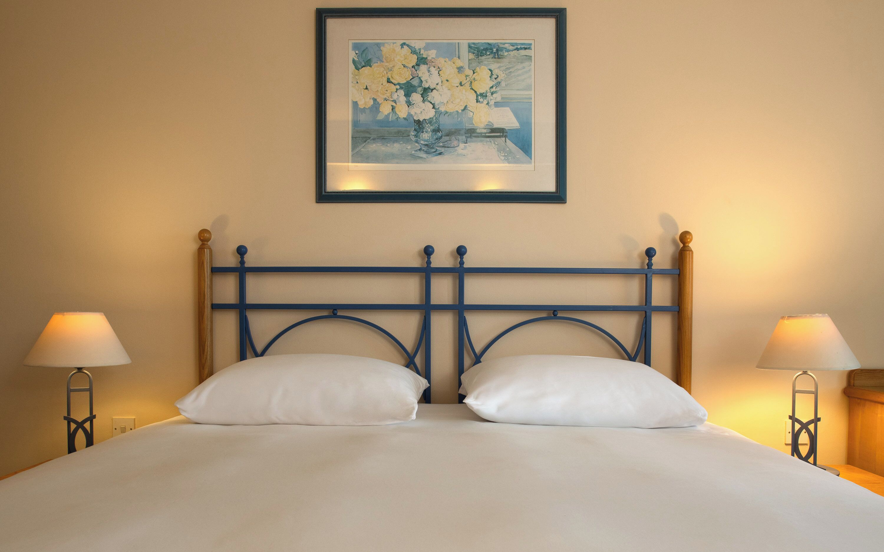 A neatly made bed with white linens, a blue metal headboard, and two bedside lamps.