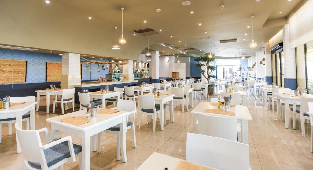Un restaurant spacieux avec des tables et des chaises blanches, un coin bar et une vue sur la ville.