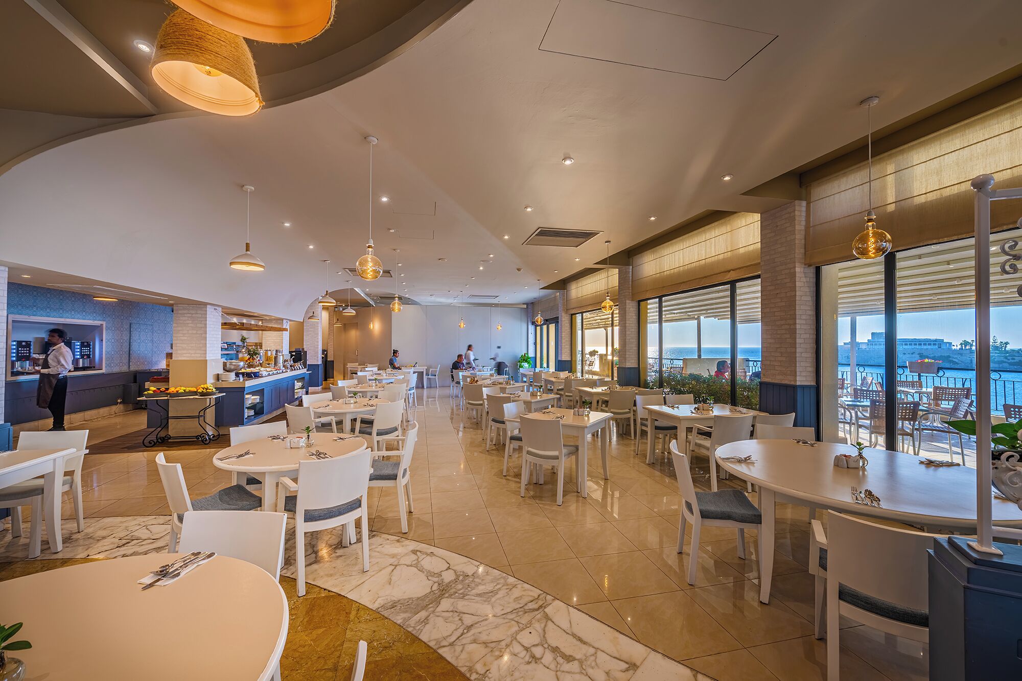 Een modern restaurant met een bar, meerdere eettafels en grote ramen met uitzicht op zee.
