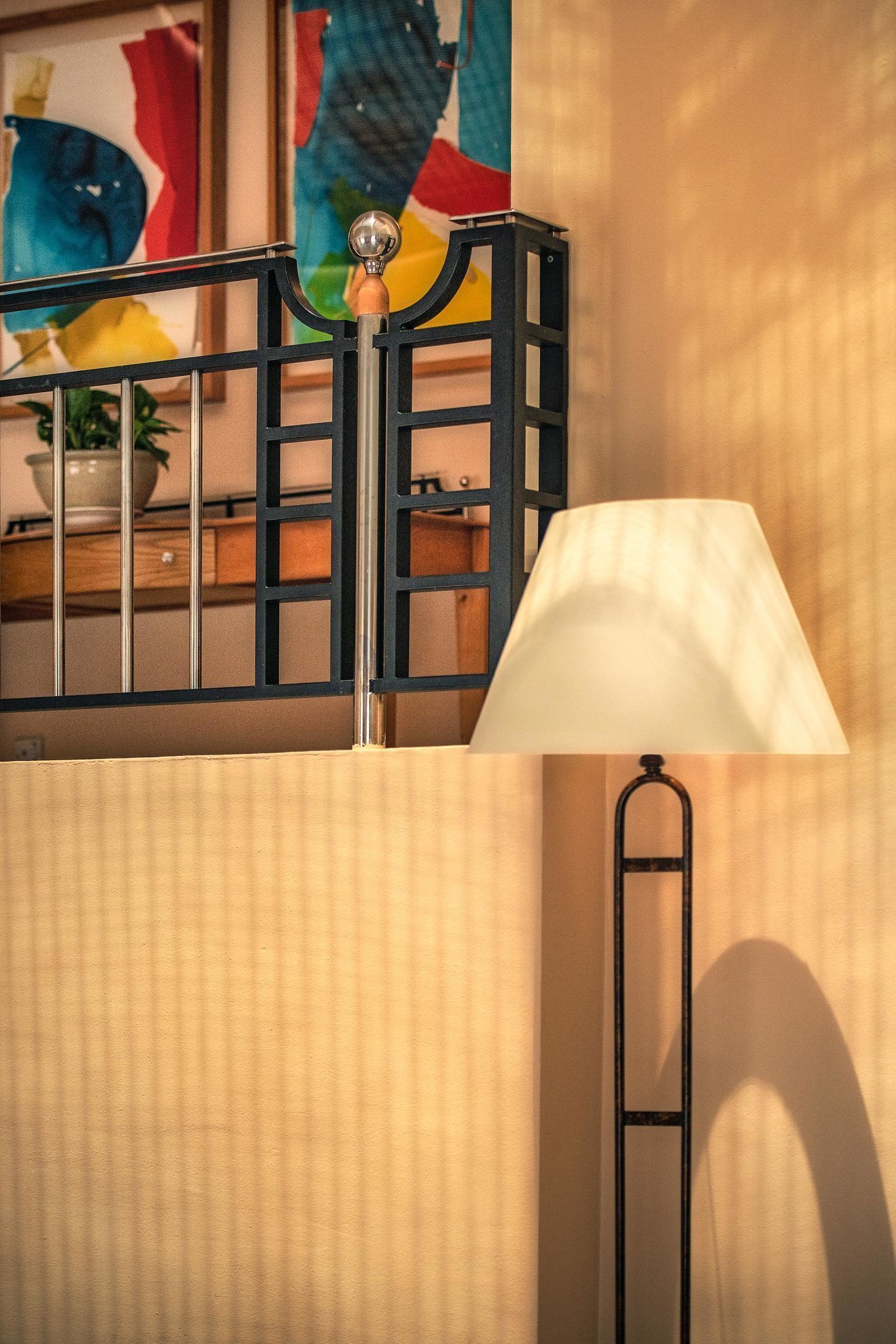 Une pièce avec une rambarde en métal noir, une lampe blanche et un tableau abstrait aux couleurs vives accroché au mur.