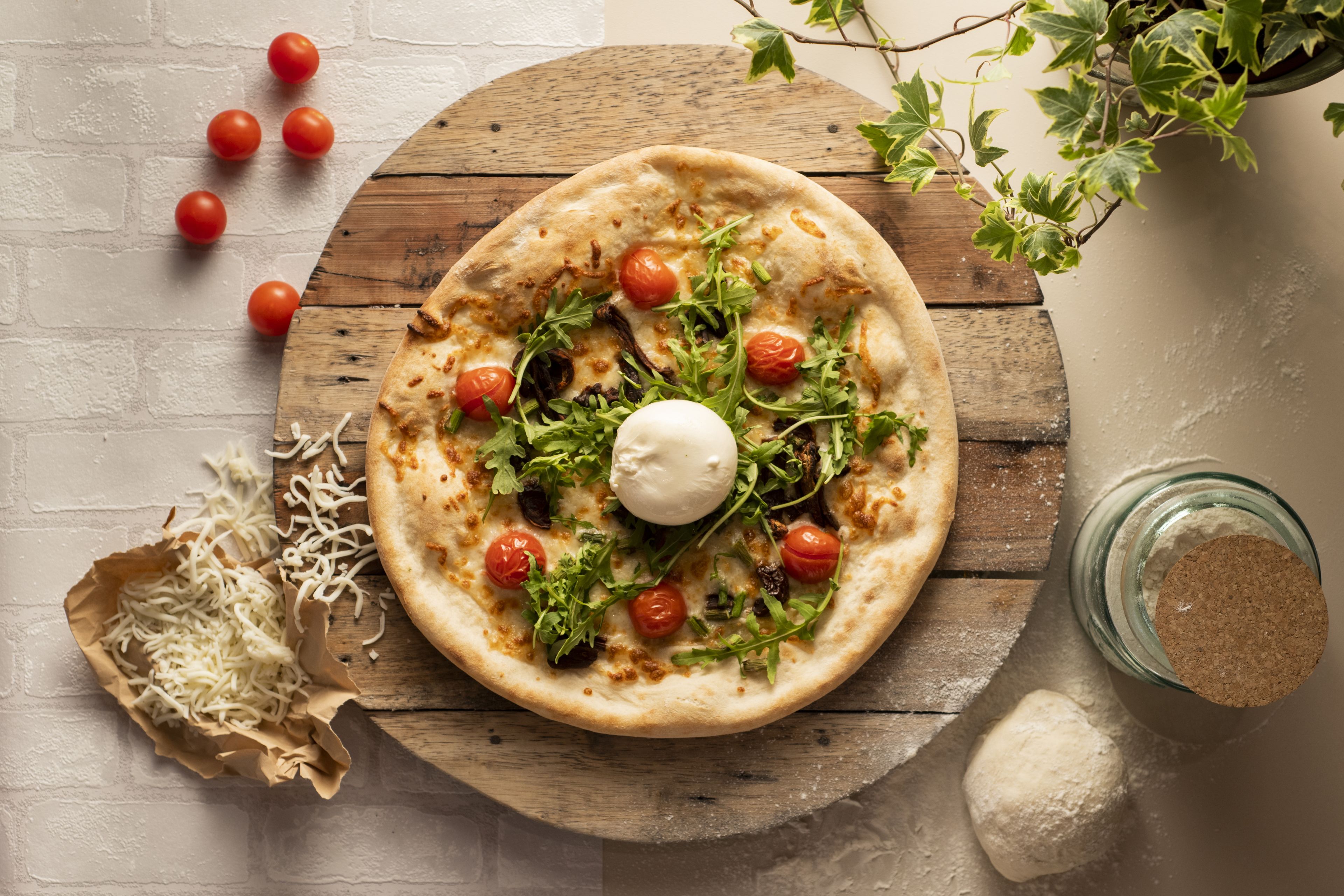 En pizza på en träbricka med tomater, grönsaker och en ostboll.