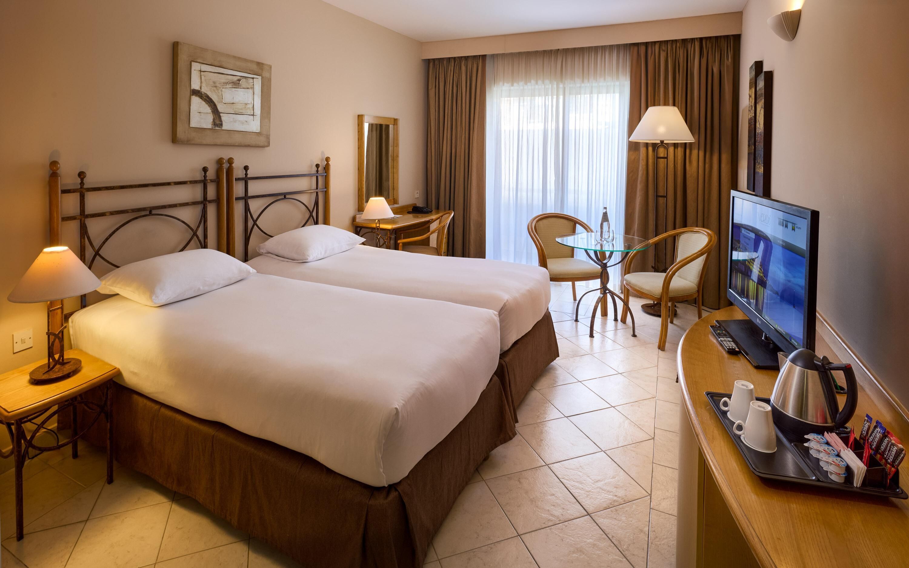 A hotel room with two beds, a desk with a computer, a TV, and a coffee station.