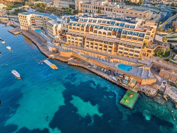 An aerial view of a coastal hotel with multiple buildings, a marina with boats, and a swimming pool.