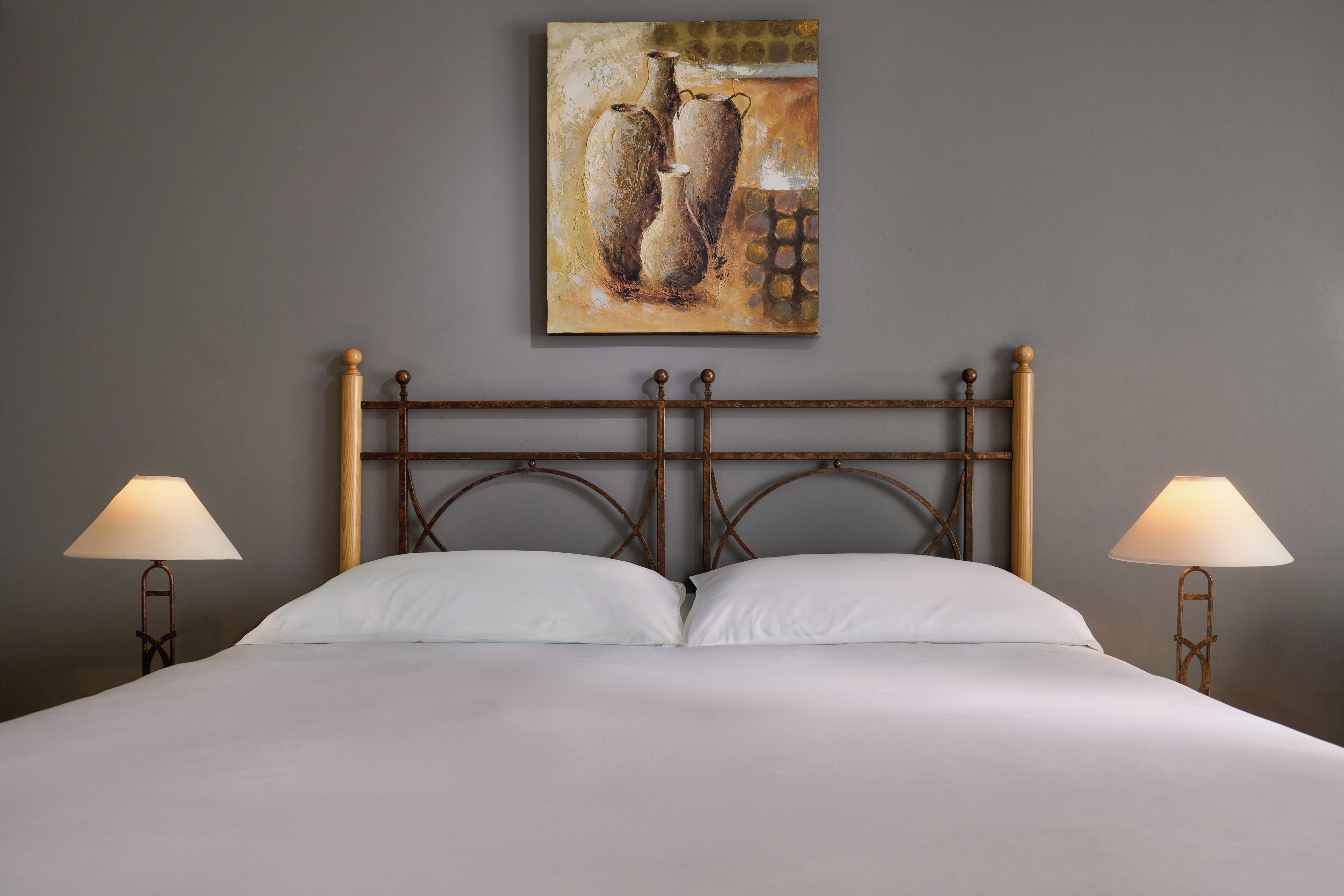 A neatly made bed with white linens, a wooden headboard, and two bedside lamps.