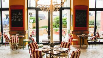 Un café con sillas y mesas a rayas, una lámpara decorativa en el centro y pizarras con mensajes.